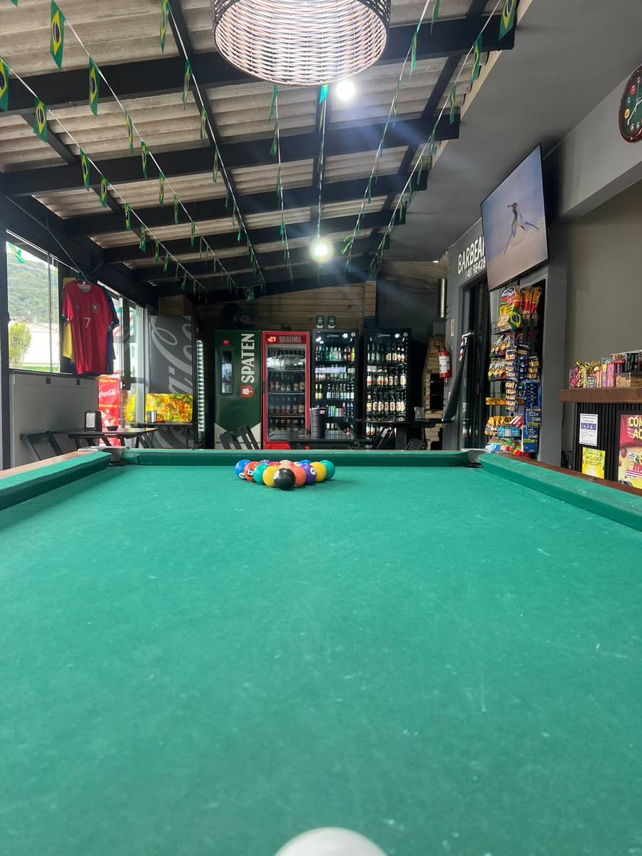 Espaço amplo e coberto do bar, com sinuca e barbearia ao fundo
